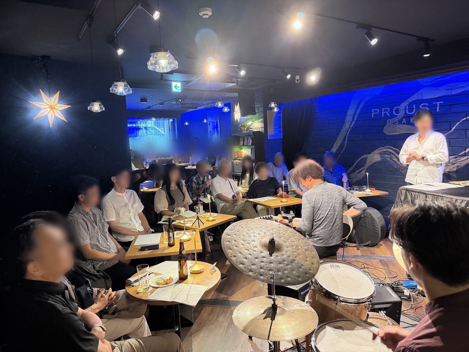 ドラムセットの後ろから見た客席。テーブル席に出演者やお客さんが座り、ステージの演奏を聴いている